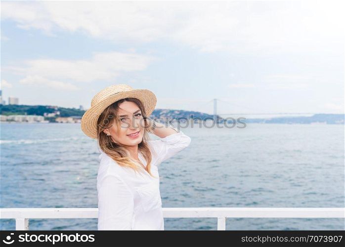 Beautiful woman cruises in a ferry with cityscape view of Istanbul Bosphorus and bridge on background.. Beautiful woman in red dress travels on a ferry in Istanbul