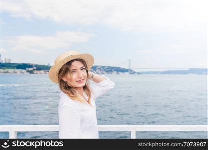 Beautiful woman cruises in a ferry with cityscape view of Istanbul Bosphorus and bridge on background.. Beautiful woman in red dress travels on a ferry in Istanbul