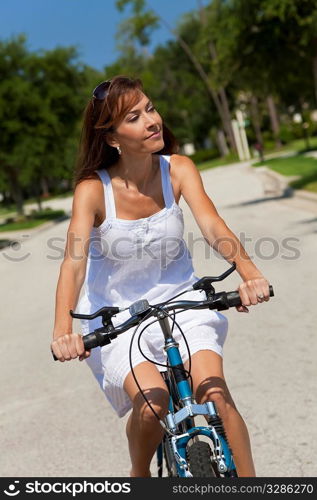 Beautiful woman cycling in a white sun dress bathed in summer sunshine