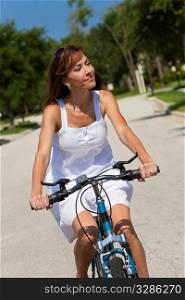 Beautiful woman cycling in a white sun dress bathed in summer sunshine