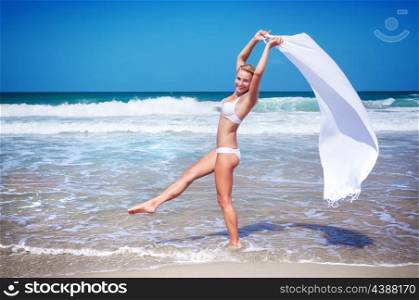 Beautiful woman dancing on the beach wearing stylish swimsuit and holding white scarf, relaxation outdoors on tropical resort, enjoying freedom and summer vacation