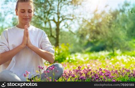 Beautiful woman doing yoga exercise outdoors, nice female in lotus pose meditate with closed eyes in beautiful blooming spring garden, healthy lifestyle, relaxation and wellness concept