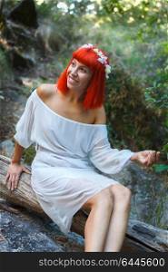 Beautiful woman dressed in white with a flower wreath sitting near to a waterfall