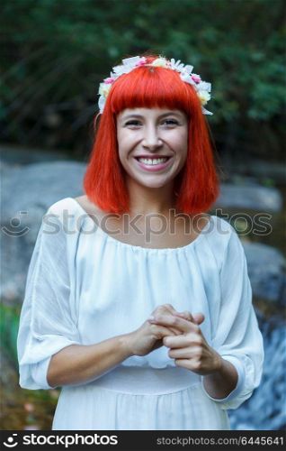 Beautiful woman dressed in white with a flower wreath sitting near to a waterfall