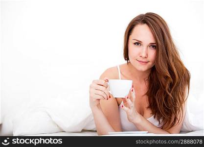 Beautiful woman drinking a coffee in her bed over white