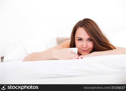 Beautiful woman drinking a coffee in her bed over white