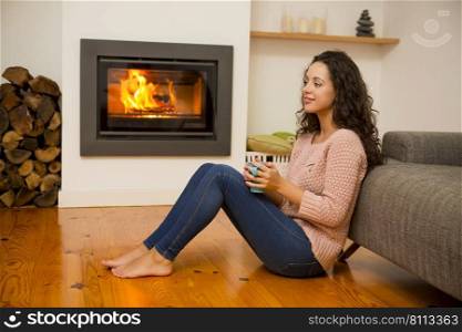 Beautiful woman drinking a hot tea at the warmth of the fireplace