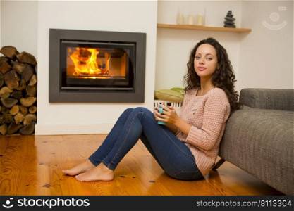 Beautiful woman drinking a hot tea at the warmth of the fireplace