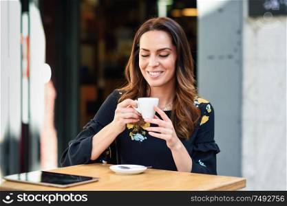 Beautiful woman drinking coffee in an urban cafe bar. Young female sitting at table at an outside terrace. Girl with california highlights hairstyle.. Middle-aged woman drinking coffee in an urban cafe bar.