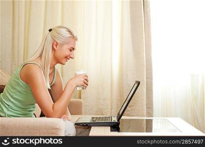 Beautiful woman drinking milk and using laptop