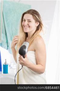 Beautiful woman drying hair in bathroom at home