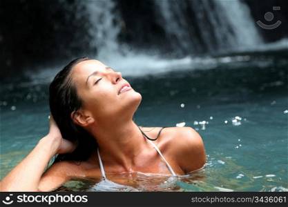 Beautiful woman enjoying bathing near natural waterfall