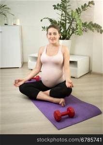 Beautiful woman expecting baby doing yoga exercise on mat at home