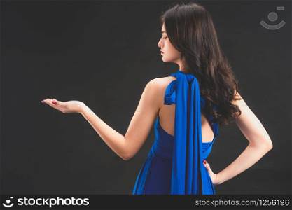 Beautiful woman fashion model in blue dress standing on dark background. Luxury advertising.