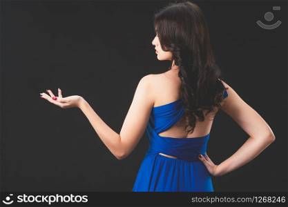 Beautiful woman fashion model in blue dress standing on dark background. Luxury advertising.