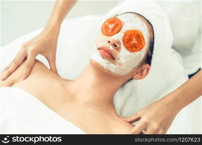 Beautiful woman having a facial mask treatment with tomato cream extract showing benefit of nature treatment. Anti-aging cosmetology, facial skin care and luxury lifestyle concept.