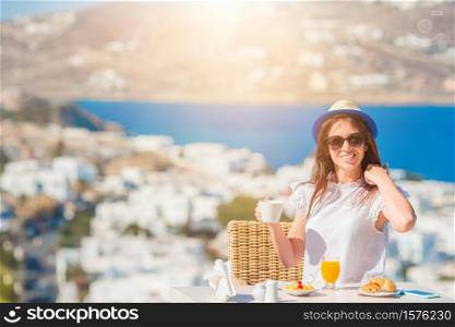 Beautiful woman having breakfast at outdoor cafe with amazing view. Girl enjoy her hot coffee early in the morning. Beautiful woman having breakfast at outdoor cafe with amazing view.