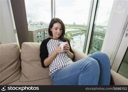 Beautiful woman having coffee on sofa at home