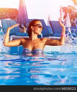 Beautiful woman having fun in the pool, making water splash by hands, enjoying hot summer day in swimming-pool, summertime holiday and vacation, refreshment concept&#xA;
