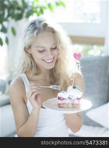 Beautiful woman having raspberry cake with fork in house