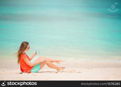 Beautiful woman holding a suncream lying on a tropical beach. Beautiful young woman holding a suncream lying on tropical beach