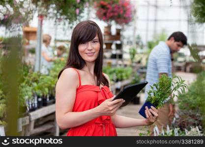 Beautiful woman holding tablet pc and potted plant with people in background