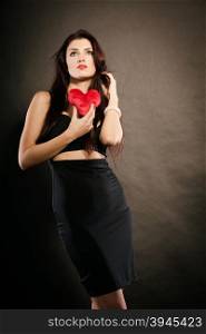 Beautiful woman holds red heart on black. Woman brunette long hair girl wearing black sensual dress holding gift in form of red heart love symbol studio shot on dark. Valentines day happiness concept