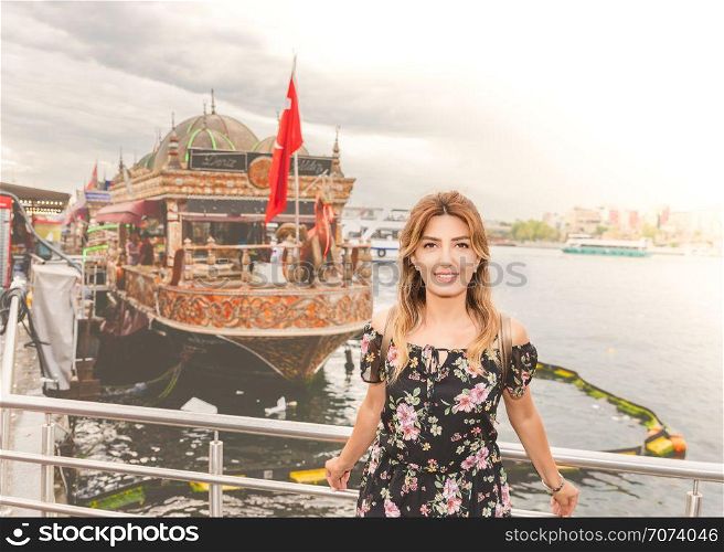 Beautiful woman in a dress stands in front of ships where grilled fish are sold in Istanbul,Turkey. Beautiful woman in a dress stands in front of ships