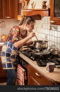 Beautiful woman in apron stirring soup with kitchen spoon