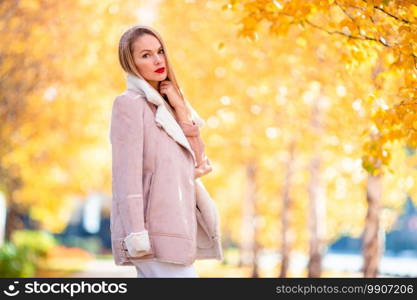 Beautiful woman in autumn park under fall foliage at warm day. Fall concept - beautiful woman drinking coffee in autumn park under fall foliage