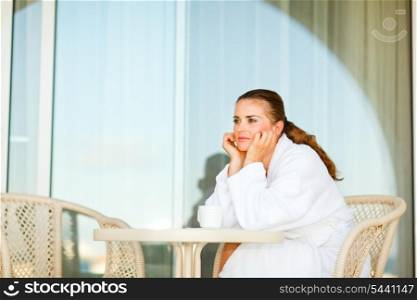 Beautiful woman in bathrobe sitting at table on terrace and dreaming