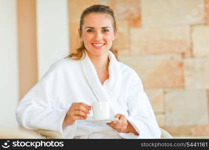 Beautiful woman in bathrobe sitting at table on terrace and having coffee