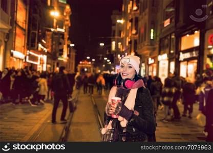 Beautiful woman in beanie with takeaway coffee and headphones uses stands at istiklal street,Istanbul