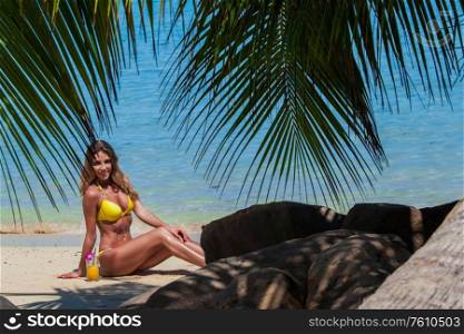 Beautiful woman in bikini sitting on sandy tropical sea beach with cocktail. Woman with cocktail on beach