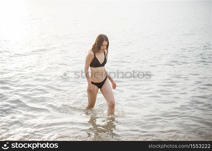 Beautiful woman in black bikini is enjoying with sea water on the beach