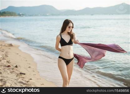 Beautiful woman in black bikini is walking on the beach