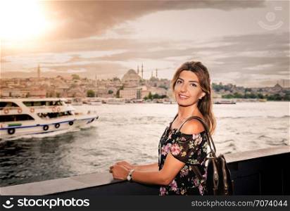 Beautiful woman in black dress stands under Galata Bridge with landscape view of Istanbul on background.. Beautiful woman in black dress stands under Galata Bridge