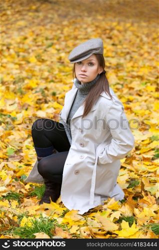 Beautiful woman in cap and white coat sitting on yellow leaf background
