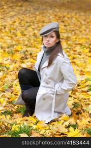 Beautiful woman in cap and white coat sitting on yellow leaf background