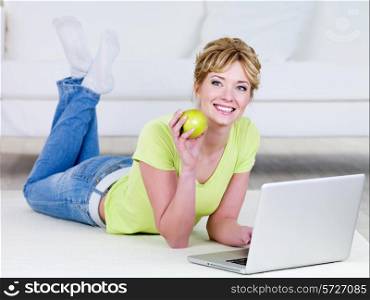 Beautiful woman in casuals with laptop eating green apple - indoors