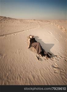 Beautiful woman in dress lying on sand dune at desert
