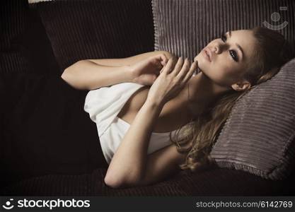 beautiful woman , in fashion portrait , she is laying on a sofa in her living room , has blond long hair ,she is looking up with dreaming expression