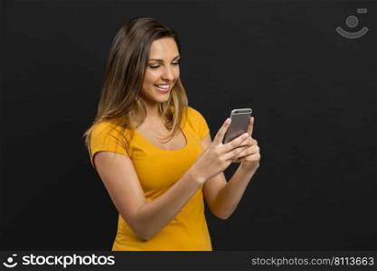 Beautiful woman in front of a dark wall texting a sms