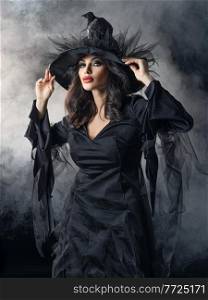Beautiful woman in Halloween witch costume dress and hat in mist. Woman in Halloween witch costume