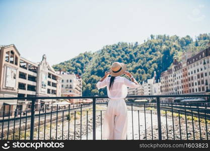 Beautiful woman in hat on the embankment of a mountain river in the city.. Happy girl at hat on the embankment of a mountain river in a European city.