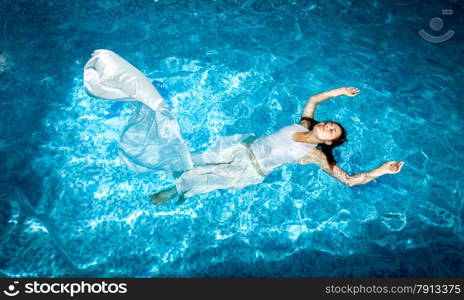 Beautiful woman in long white dress swimming in pool at sunny day