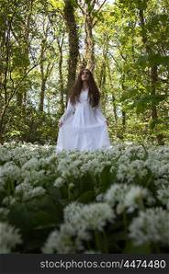 Beautiful woman in long white medieval dress standing in a forest looking upwards