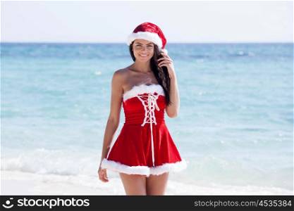 Beautiful woman in Mrs. Claus custume on tropical beach, Christmas vacations concept