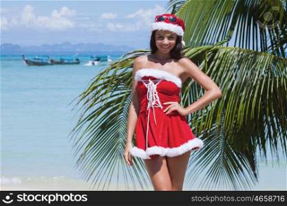 Beautiful woman in Mrs. Claus custume on tropical beach with palms, Christmas vacations concept