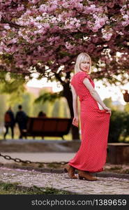 beautiful woman in red dress in the city near flowering trees. Outdoor portrait of young beautiful happy smiling girl with red lips, short hair, posing near blooming tree. Copy, empty space for text.. beautiful woman in red dress in the city near flowering trees. Outdoor portrait of young beautiful happy smiling girl with red lips, short hair, posing near blooming tree. Copy, empty space for text